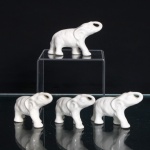 Quatro(04) elefantes em porcelana branca esmaltada, representados em posição de marcha, com trombas erguidas e modelagem simplificada. Superfície monocromática, com detalhes anatômicos definidos em relevo, incluindo orelhas, olhos e pregas do corpo. Peças reunidas em conjunto. Medidas: Alt.: 4,5 x Comp.: 8 x Larg.: 2,5cm.