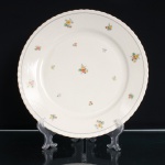 Count Thun Porcelain Factory, Kláterec - República Tcheca(Fundada em 1794). Prato para bolo executado em porcelana, com esmaltação em tonalidade marfim, aba larga e bordo suavemente ondulado. Decoração policromada composta por pequenos ramalhetes florais distribuídos pelo centro e pela aba, em tonalidades de amarelo, laranja, verde, azul e cinza, delimitada por filete perimetral cinza. No reverso, marca de manufatura sob coroa, com as inscrições TK, Thun e Czechoslovakia, correspondentes à manufatura Thun, Tchecoslováquia. Primeira metade do século XX. Medida: Diam.: 30cm.