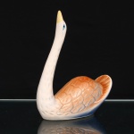 Escultura de cisne executada em cerâmica esmaltada. Figura moldada com pescoço alongado e arqueado, bico em amarelo e olhos em azul e preto. Corpo com plumagem estilizada em relevo, formada por sucessão de penas incisas, sob esmaltação em tonalidades de branco, azul e ocre-alaranjado, aplicada em gradação. Cauda elevada com sulcos longitudinais. Base oval, vazada no reverso, com interior esmaltado. Sem marca de manufatura. Medidas: Alt.: 24 x Comp.: 19 x Larg.: 9,5 cm.