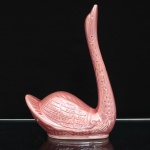 Escultura de cisne em cerâmica esmaltada. Figura moldada com pescoço alongado e erguido, corpo de linhas estilizadas e cauda elevada. Plumagem trabalhada em relevo, com sucessão de penas e incisões distribuídas pelas asas, corpo e pescoço. Revestimento integral por esmalte rosa, com variações de tonalidade decorrentes da aplicação e da modelagem. Base oval vazada, sem marca de manufatura. Medidas: Alt.: 28,5 x Comp.: 20 x Larg.: 10 cm.