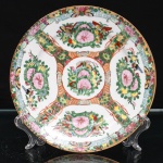 Prato de coleção em porcelana chinesa de exportação, estilo família rosa, Cantão, Dinastia Qing. Decorado em esmaltes policromos sobre o vidrado, com predominância de rosa, verde, amarelo, azul, vermelho-ferro e preto, acrescidos de douração. Composição organizada em reservas radiais: medalhão central com flores, frutos e borboletas; quatro cartelas maiores com peônias, frutos, folhagem e insetos, intercaladas por campos preenchidos por motivos florais e elementos arquitetônicos. Aba ornamentada por friso de meandro em azul-celeste, reservas florais, borboletas e ramos sobre fundo dourado. Filete em douradura percorre o bordo. No verso, marca de quatro caracteres em esmalte vermelho-ferro, inscrita em cartela quadrangular. Medida: Diam.: 20,5cm.