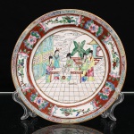 Prato de aparato em porcelana chinesa, estilo Cantão, decoração famille rose. Ornamentação em esmaltes policromos sobre o vidrado, com douração. Ao centro, cena de interior palaciano representando figuras femininas reunidas em torno de mesa, dedicadas à pintura e à caligrafia, acompanhadas por serviçais, entre elementos arquitetônicos, mobiliário e vegetação. Aba organizada em reservas com aves, flores e frutos, alternadas com composições florais sobre fundo vermelho; faixa externa percorrida por friso de meandros policromos. Bordo contornado por filete a ouro. No verso, marca apócrifa Qianlong em vermelho-ferro, com a inscrição "Qianlong nian zhi", "Feito durante o reinado de Qianlong". Medida: Diam.: 19,5 cm.