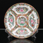 Prato de coleção em porcelana chinesa, estilo Cantão, decoração famille rose. Ornamentação em esmaltes policromos sobre o vidrado, com douração. Composição estruturada em quatro reservas lobuladas, preenchidas por peônias, frutos, aves e borboletas, dispostas em torno de medalhão central com motivos florais e ornitológicos. Os intervalos são ocupados por ramagens, florações, frutos e elementos geométricos realçados a ouro. Aba percorrida por friso de meandros, intercalado por motivos florais e borboletas. Bordo contornado por filete a ouro. No verso, marca apócrifa Qianlong em vermelho-ferro, com a inscrição "Qianlong nian zhi", Feito durante o reinado de Qianlong, em referência ao imperador Qianlong(17361795), da dinastia Qing. Medida: Diam.: 20,5 cm.