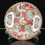 Prato de coleção em porcelana chinesa, estilo Cantão, decoração famille rose, tipo Rose Medallion. Ornamentação em esmaltes policromos sobre o vidrado, com douração. Composição compartimentada em reservas figurativas, representando mulheres em interiores e varandas de arquitetura chinesa, alternadas com cartelas de peônias, frutos, aves e borboletas. Medalhão central com figura feminina sentada diante de mesa, inserido em campo vermelho pontuado por florações e circundado por quatro reservas botânicas. A aba reúne cenas domésticas, medalhões com caracteres auspiciosos, motivos florais, aves e insetos sobre fundo dourado. Bordo circundado por por filete a ouro. No verso, marca apócrifa Qianlong em vermelho-ferro, com a inscrição "Qianlong nian zhi", "Feito durante o reinado de Qianlong", em referência ao imperador Qianlong(1736-1795), da dinastia Qing. Marcas dessa inscrição continuaram a ser empregadas em porcelanas posteriores, inclusive no século XX. Medida: Diam.: 20 cm.
