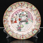 Prato de aparato em porcelana chinesa, estilo Cantão, decoração famille rose, tipo Rose Medallion. Ornamentação em esmaltes policromos sobre o vidrado, com douração. Ao centro, cena de interior representando quatro figuras femininas reunidas em torno de tabuleiro do jogo Go(weiqi), acompanhadas por serviçal, entre mobiliário, cortinados, elementos arquitetônicos e vaso com flores. Aba compartimentada por medalhões contendo frutos, flores e aves, intercalados por reservas reticuladas, peônias, folhagens, meandros e ornatos a ouro. A cena central integra o repertório chinês de representações das artes e passatempos eruditos, no qual o weiqi figura entre as chamadas Quatro Artes do letrado. Bordo contornado por filete dourado. No verso, marca apócrifa Qianlong em vermelho-ferro, com a inscrição "Qianlong nian zhi", Feito durante o reinado de Qianlong, em referência ao imperador Qianlong(1736-1795), da dinastia Qing((1736-1795). Medida: Diam.: 19,5 cm.