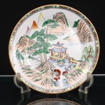 Prato de aparato em porcelana chinesa, decoração famille rose. Ornamentação em esmaltes policromos sobre o vidrado, com douração. Ao centro, paisagem montanhosa de inspiração shan shui, composta por formações rochosas, pinheiros, salgueiro, cursos dágua e pavilhão sobre as águas, ligado à margem por passadiço, com figuras em seu interior. Ao longe, picos montanhosos emergem entre planos sucessivos da paisagem. Aba estreita ornamentada por sequência de flores, frutos e folhagens sobre fundo dourado, delimitada internamente por friso geométrico. Bordo contornado por filete a ouro. No verso, marca apócrifa Qianlong em vermelho-ferro, com a inscrição "Qianlong nian zhi", "Feito durante o reinado de Qianlong", alusiva ao reinado de Qianlong(1736-1795), dinastia Qing.Medida: Diam.: 27cm.