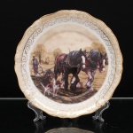 Prato decorativo executado em porcelana, coleção Rural Life Collection, bordo recortado, aba moldada em relevo com acabamento em tonalidade marfim perolada, rematada por filetes dourados. Ao centro, reprodução em estampagem policromada de composição campestre assinada Peter Goodhall, representando lavrador conduzindo arado tracionado por dois cavalos de trabalho, acompanhado por cão, em paisagem rural. A composição é circundada por faixa de arabescos dourados. No verso, inscrições "RURAL LIFE COLLECTION - Under The Tree". Medida: Diam.:  25,5cm.