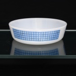 Travessa refratária circular em vidro opalino, de tonalidade branco leitoso, decorada com faixa geométrica em azul, composta por padronagem quadriculada alternando campos lisos e reticulados, padrão dito "xadrez". Fabricado no Brasil pela empresa Brasividro S.A., sob a marca Termo-Rey, durante a década de 1970. No verso, marca moldada com símbolo da manufatura, numeração "5" e inscrições "Termo-Rey", "MADE IN BRAZIL" e "BRASIVIDRO". Medidas: Alt.: x Diam.: