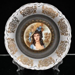 Fruteira em porcelana nacional, formato circular de perfil raso, aba de contorno recortado, moldurada em relevo e rematada por filete dourado. Decoração policroma composta por arranjo floral central, com rosas e demais flores em tonalidades rosa, azul, amarelo e alaranjado, entre folhagens verdes; motivos florais menores distribuídos pela aba, sobre fundo de tonalidade prateada e cinza. Campo delimitado por filete dourado. Verso apresenta suporte metálico para suspensão. Marca da manufatura no verso, não identificada. Medidas: Alt.: x Diam.: