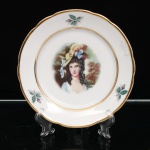 Porcelana Real, Mauá - SP(Fundada em 1943 por Fritz Erwin Schmidt). Prato de coleção em porcelana nacional, esmaltagem vítrea na cor branca, aba recortada e contornada por filete dourado. Centro ornado com reprodução em estampagem policromada do retrato de Georgiana Cavendish, Duquesa de Devonshire (1757-1806), segundo composição de Thomas Gainsborough (1727-1788), representada em traje azul, cabelos dispostos em cachos e chapéu com plumas e laços. A figura é enquadrada por paisagem em tonalidades de verde e castanho, acompanhada da inscrição Gainsborough by Joh. Peter, Amsterdam-Holland. Marca da manufatura no verso. Medida: Diam.: