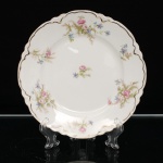 Johnson Brothers, Hanley  Inglaterra(fundada em 1883 pelos irmãos Alfred, Frederick e Henry Johnson). Prato em faiança inglesa de tonalidade marfim, aba recortada em segmentos lobulados e bordo contornado por filete dourado. Decoração floral policroma, composta por rosas em tonalidades de rosa e branco, flores azuis, folhagens verdes e ramagens. No verso, marca estampada em verde sob coroa, com as inscrições "JOHNSON BROS / ENGLAND / RD. No. 9955". Apresenta dispositivo metálico para suspensão. Medida: Diam.: