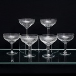 Conjunto de seis(06) taças em meio cristal incolor,bojo em formato de coupe,  dotado de ornamentação executada em gravação, organizada em faixas concêntricas: friso superior de elementos lanceolados sucessivos e, abaixo, composição contínua de volutas, círculos e entrelaçamentos geométricos. Medidas: Alt.: x Diam.: