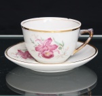 PORCELANA RAMI, Jundiaí  São Paulo (fundada em 1930). Xícara para chá em porcelana nacional, de esmaltação branca, decoração floral em estampagem policromada, representando orquídeas em tonalidades rosa, verde e amarelo. Bojo hemisférico assente sobre base circular, com alça lateral angular realçada por douradura; pires circular de aba ligeiramente côncava, ornamentado pelo mesmo motivo botânico. Bordas e cavidade de assentamento delimitadas por frisos dourados. Marca de manufatura PORCELANA RAMI na base. Estado conforme fotografias. Medidas: Xícara: Alt.: 5,5 x Diam.: 8,5 ; Pires: Diam.:13,5cm.