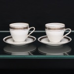 Porcellana Mauá, Mauá - SP(Fundada em 1937 por Fritz Erwin Schmidt / ativa até 1968). Duas(02) xícaras para café em porcelana nacional, esmaltagem vítrea na cor branca, decorada com faixa contínua de meandro grego, executada em tonalidade prateada, bojo oval e alça lateral em voluta, padrão decorativo replicado no pires. Marca da manufatura no verso. Medidas: Xícara: Alt.: x Comp.: x Larg.: ; Pires: Diam.: