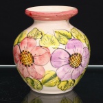 Vaso executado em faiança, corpo globular, colo curto e boca circular de bordo espessado. Superfície esmaltada em tonalidade marfim, com decoração floral policroma aplicada à mão, composta por flores em rosa e lilás, centros em amarelo e laranja, folhagem em verde e contornos em preto; faixa do gargalo na tonalidade magenta. Apresenta fraturas no bordo e no colo, com intervenção de restauro, conforme registro fotográfico. Medidas: Alt.: x Diam.: