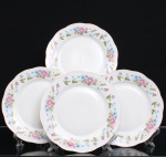 Conjunto de quatro(04) pratos rasos em porcelana, esmaltação branca, aba recortada em segmentos e filete perimetral em dourado. Decoração em estampagem policromada composta por ramagens dispostas sobre a aba, com flores em tonalidades rosa, azul e bege, folhagem verde e elementos fitomórficos em ocre, interligados por hastes sinuosas. Medida: Diam.: