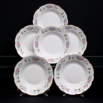 Conjunto de seis(06) pratos rasos em porcelana, esmaltação branca com decoração floral em estampagem policromada disposta sobre a aba, composta por flores em tonalidades de rosa, azul e ocre, articuladas por ramos, folhagens verdes e elementos fitomórficos. Aba de contorno festonado, rematada por filete dourado. Medida: Diam.: