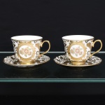 Duas(02) xícaras para chá em porcelana, bojo campaniforme, assente sobre pequeno pé anular, com alças arqueadas e esmaltação branca. Superfície externa revestida por generosa composição em douradura, organizada em reservas circulares com arranjos florais policromos em tons de rosa, verde e azul, entre motivos fitomórficos estilizados. Pires com ornamentação correspondente, centrada por medalhão floral. Bordos, bases e alças realçados a ouro. Medidas: Xícara: Alt.: x Comp.: x Larg.: ; Pires: Diam.: