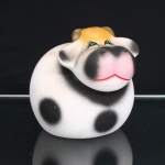 Pote / biscoiteira executado em cerâmica na forma de vaca, recipiente moldado com corpo globular e abertura superior circular, encimada por tampa modelada em forma de cabeça, com focinho proeminente, orelhas laterais e chifres. Superfície esmaltada em branco, com manchas pretas aplicadas por aerografia; cabeça com detalhes em preto, rosa, verde, amarelo e vermelho, incluindo olhos delineados, pelagem frontal, focinho e boca. Tampa removível com encaixe sobre a abertura do recipiente. Sem marca de manufatura. Medidas: Alt.: 15,5 x Comp.: 18 x Larg.: 14 cm.