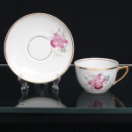 PORCELANA RAMI, Jundiaí  São Paulo (fundada em 1930). Xícara para chá em porcelana nacional, de esmaltação branca, decoração floral em estampagem policromada, representando orquídeas em tonalidades rosa, verde e amarelo. Bojo hemisférico assente sobre base circular, com alça lateral angular realçada por douradura; pires circular de aba ligeiramente côncava, ornamentado pelo mesmo motivo botânico. Bordas e cavidade de assentamento delimitadas por frisos dourados. Marca de manufatura PORCELANA RAMI na base. Medidas: Xícara: Alt.: 5 x Comp.: 10,5 x Larg.: 8,5cm. ; Pires: Diam.: 13,5cm.