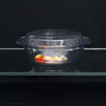 Assadeira redonda com tampa em vidro refratário, linha Marinex - Santa Marina, Brasil. Recipiente circular, base plana e duas alças laterais integradas destinadas ao manuseio, acompanhado de tampa ajustada, igualmente provida de abas. Executado em vidro incolor destinado ao uso em forno e à apresentação de alimentos à mesa. Conserva etiqueta circular de fábrica com as inscrições "Qualidade Santa Marina  Marinex  Vidro para Forno  Assadeira Redonda com Tampa" e o lema "Do forno para a mesa, da mesa para a geladeira", além da marca "MARINEX" moldada ao fundo. Medidas: Alt.: 10 x Comp.: 27 x Larg.: 23 cm.