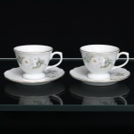 Porcelana Schmidt, Santa Catarina, Brasil (Fundada em 1945). Duas(02) xícaras para café em porcelana nacional, linha Classic, esmaltação na cor branca, bojo campaniforme sobre pé circular alteado, com asas arqueadas; pires de contorno lobulado. Decoração floral composta por rosas brancas, centros em tonalidade salmão e folhagem verde, com contornos parcialmente realçados em relevo. Filetes dourados percorrem os bordos. No verso, marca de manufatura "Porcelana Schmidt  Classic  Brasil", acompanhada do emblema. Medidas: Xícara: Alt.: 5 x Comp.: 8,5 x Larg.: 7cm. ; Pires: Diam.: 10,5cm.