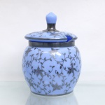 Potiche de servir / poncheira de mesa com tampa em vidro opalinado acetinado (vidro Bristol) na cor azul-celeste. Decoração em sobreposição metálica(silver overlay). Provável manufatura europeia(Inglaterra ou Boêmia), meados do século XX, c.1940-1960). Formato bojudo ovoide e boca circular guarnecida por aro de metal espessado. Toda a superfície exterior do bojo e da tampa é ricamente ornamentada por uma intrincada aplicação de sobreposição em prata ou liga metálica prateada, figurando ramagens sinuosas, gavinhas e flores estilizadas, tampa removível de perfil convexo apresenta uma abertura/reentrância lateral para encaixe de concha de servir, sendo encimada por grande pomo torneado facetado. Sem marcação visível de manufatura. Dimensões: 27 cm de altura x 19 cm de diâmetro (considerando a tampa).