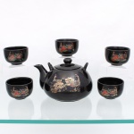 Serviço de chá oriental em porcelana esmaltada de tonalidade preto brilhante, composto por seis(06) peças: Um bule com tampa e cinco xícaras de servir(bowl). Produzido em Taiwan, (c. 1970-1990). Apresentam corpo robusto de formato arredondado, inteiramente recoberto por espesso esmalte preto com alto brilho, face frontal exibe rica  ornamentação transferida por decalcografia e realçada em policromia com interferência de douração, figurando um casal de pavões imperiais estilizados entre grandes peônias e ramagens floridas orientais; bule apresenta bico vertedor curto curvo, tampa removível de encaixe anatômico com pomo cilíndrico e duas pequenas alças superiores perfuradas integradas ao ombro da peça(para encaixe de alça flexível de bambu ou meta), xícaras ostentam o mesmo padrão decorativo texturizado em escala menor, com bocal liso de perfil circular e base anelar. Verso inferior do bule, apresenta marca da manufatura gravada em relevo sob o esmalte com um monograma estilizado figurando a letra "M" emoldurada por uma serpente ou cisne em arco, acompanhada pelo símbolo de marca registrada. No reverso inferior das xícaras, ostenta a inscrição de procedência geográfica em relevo: "TAIWAN". Medidas: Alt.: x Comp.: x Larg.: cm; Medidas: Alt.: x Diam.: cm.