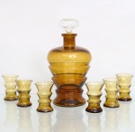Serviço para licor em vidro moldado na tonalidade âmbar. Composto por sete(07) peças: uma garrafa licoreira com tampa e seis minicopos . Apresentam sinuoso design geométrico vintage de linhas modulares escalonadas, garrafa ostenta bojo robusto tripartido por anéis horizontais em relevo, gargalo curto com boca circular evertida e base em pedestal combinante, acompanhada por sua tampa original em formato oval de perfil achatado, cujo pino inferior cônico se ajusta perfeitamente ao gargalo. Os seis copinhos seguem estritamente a mesma proposta estética modular da garrafa em escala reduzida, exibindo corpo cintado por anéis salientes, bocal evertido e base espessa. Medidas: Garrafa: Alt.: x Diam.: cm. Copos: Alt.: x Diam.: cm.