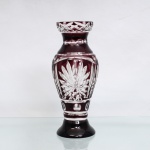 Vaso em cristal doublé de translúcido e vinho, corpo balaústre, decoração obtida por lapidação profunda, com remoção seletiva da camada cromática, formando reservas transparentes compostas por motivos radiais, lancetas, losangos, facetas ovais e frisos geométricos. Colo estrangulado, boca circular com faixa lapidada em padrão entrecruzado e base circular alargada. Medidas: Alt.: x Diam.: cm.