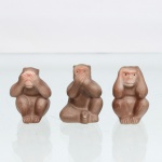 Conjunto de Esculturas representando "Três Macacos Sábios" cerâmica moldada e fosca.  Representando o clássico provérbio místico oriental ("não veja o mal, não fale o mal, não ouça o mal"), figurados por primatas sentados em posições tradicionais. Acabamento texturizado em tom marrom-argila acetinado com sombreados escuros e detalhes sutis de policromia rosada nas faces e extremidades. Fundo plano com orifício técnico de escoamento e numerações de inventário antigas manuscritas à tinta ("241"). Medidas: Alt.: x Comp.: x Larg.: cm.