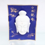 Placa decorativa em porcelana esmaltada, de formato retangular vertical e perfil levemente ondulado, com fundo azul-cobalto e contorno em dourado. Ao centro, aplicação em alto-relevo de cabeça de Guanyin (Kuan Yin) em porcelana branca, representada com olhos semicerrados, lóbulos auriculares alongados e cabelos reunidos em coque, ornamentados por motivo floral. Campo decorado com inscrições em caracteres chineses dourados, incluindo Baiyi Guanyin, Guanyin de Vestes Brancas, uma das representações da bodhisattva da compaixão. Verso provido de cordão para suspensão. Medidas: Alt.: 24 x Comp.: 19 x Larg.: 7,5cm