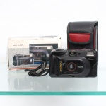 Câmera fotográfica analógica Yashica, Japão. Câmera compacta para filme 35 mm, corpo em material sintético preto, dotada de objetiva focus-free, visor óptico, flash eletrônico integrado e seletor de sensibilidade ISO 100400. Inscrição frontal "Yashica" e "Focus-Free  Lens Made in Japan". Compartimento posterior para filme com avanço e rebobinamento manuais. Acompanha estojo, alça de pulso e embalagem original identificada "35mm Camera". Apresenta sinais de uso, riscos e perdas no acabamento, com desgaste mais acentuado na região superior do corpo. Funcionamento não verificado.