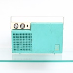 Toca-discos portátil com rádio integrado - Sanyo do Brasil, década de 1970. Aparelho portátil, com gabinete em material sintético de tonalidade turquesa e creme, tampa articulada e alça para transporte. Reúne toca-discos e receptor de rádio em um único conjunto, com alto-falante incorporado. Plataforma fonográfica com prato circular, braço reprodutor e seletor de velocidades 33, 45 e 78 rpm; painel frontal dotado de comandos de acionamento, sintonia e seletor "Fono/Rádio", com recepção em ondas médias (AM). No reverso, inscrição moldada Indústria Eletrônica Sanyo do Brasil Ltda.  Indústria Brasileira. A empresa brasileira da Sanyo foi constituída em São Paulo em 1970, dado compatível com a atribuição do aparelho à década de 1970. Apresenta marcas de uso, sujidades e alterações superficiais decorrentes do tempo. Funcionamento não verificado. Medidas: Alt.: x Comp.: x Larg.: cm.
