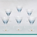 CRISTAL HERING - BLUMENAU. Elegante conjunto de taças para champanhe em cristal, fabricação nacional, circa 1960-70. Bojo de formato obcônico com transição cromática na tonalidade azul-baikal translúcida na porção inferior, terço superior exibe lapidação em sulcos verticais paralelos, fuste hexagonal sobre base circular. Composto de seis(06) unidades. Três exemplares conservam as etiquetas de manufatura originais. Medidas: Alt.: 14 x Diam.: 10 cm.