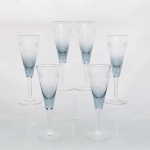 CRISTAL HERING - BLUMENAU. Elegante conjunto de taças tipo flûte para espumante em cristal, fabricação nacional, circa 1960-70. Bojo de formato obcônico com transição cromática na tonalidade azul-baikal translúcida na porção inferior, terço superior exibe lapidação em sulcos verticais paralelos, fuste hexagonal sobre base circular. Composto de seis(06) unidades. Medidas: Alt.: 14 x Diam.: 10 cm.