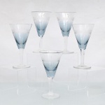 CRISTAL HERING -BLUMENAU. Elegante conjunto de taças para vinho tinto em cristal, fabricação nacional, circa 1960-70. Bojo de formato obcônico com transição cromática na tonalidade azul-baikal translúcida na porção inferior, terço superior exibe lapidação em sulcos verticais paralelos, fuste hexagonal sobre base circular. Composto de cinco(05) unidades. Dois exemplares conservam as etiquetas de manufatura originais. Medidas: Alt.: 13,5 x Diam.: 7 cm.