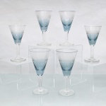 CRISTAL HERING - BLUMENAU. Elegante conjunto de taças para vinho dom Porto em cristal, fabricação nacional, circa 1960-70. Bojo de formato obcônico com transição cromática na tonalidade azul-baikal translúcida na porção inferior, terço superior exibe lapidação em sulcos verticais paralelos, fuste hexagonal sobre base circular. Composto de seis(06) unidades. Medidas: Alt.: 12 x Diam.: 6 cm.