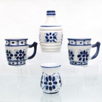 Porcelana Monte Sião, Monte Sião - MG. Duas(02) canecas, uma(01) garrafa e um(01) pequeno vaso, moldados em porcelana branca e decorados com pintura em azul-cobalto, formando flores, folhas, pontos e frisos; garrafa apresenta corpo anelado, painéis florais e gargalo curto;  canecas com alças angulares e faixas ornamentais; o vaso adota perfil abaulado com boca expandida. Marca da manufatura ao fundo. Medidas: