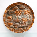 Prato decorativo de parede em metal repuxado e relevado, acabamento acobreado. Formato circular com composição em relevo representando paisagem tropical, com cabanas de cobertura vegetal, coqueiros, cercas, caminhos, pequenas embarcações e elevações ao fundo. Campo central executado por repuxo e cinzelagem, com diferentes texturas para a representação do terreno, vegetação, água e elementos arquitetônicos. Aba larga ornamentada por friso de esferas e sucessão de motivos semicirculares em relevo, com bordo ondulado. No reverso, contém gancho para suspensão. Medida: Diam.: