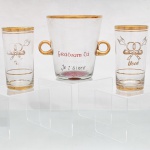 Conjunto comemorativo de casamento em vidro. Composto por uma(01) balde para gelo e dois(02) copos long drink. Decoração por aplicação dourada, com frisos no bordo e motivos de alianças entrelaçadas, laço e aves em voo, acompanhados de inscrições alusivas ao vínculo afetivo em diferentes idiomas, entre elas "Você" e "Je taime". Medidas: