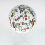 Prato de parede decorativo em porcelana chinesa de Jingdezhen, estilo Família Rosa, circa meados do século XX. O centro de fundo branco apresenta composição policromada esmaltada com os "Cem Insetos" (Baichong), destacando três grandes borboletas (hudie) dispostas perifericamente e cercadas por grinaldas sinuosas de ramificações fitomórficas, botões e flores diversas entrelatadas por fitas. O reverso exibe base anelar, fixação artesanal superior de passador metálico(adaptado) triangular por meio de massa adesiva(durepox) cinza para suspensão em parede e marca de manufatura carimbada em tom vermelho contendo caracteres chineses sobrepostos às inscrições  "Made in China". Medidas: Alt.: 3,5 x Diam.: 14cm.