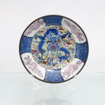 Prato de parede decorativo em porcelana chinesa com guarnição em latão, estilo Família Rosa (Cantão), circa meados do século XX. Apresenta ao centro decoração policromada representando um dragão imperial esmaltado nos tons de azul, vermelho e verde entre nuvens estilizadas. A aba é subdividida por quatro reservas que alternam painéis geométricos em azul sob o vidrado e representações de fênix (fenghuang) em tom rosa. O reverso exibe estrutura externa em latão que recobre o bordo, dotada de passador para suspensão em parede, além de fundo com marca de manufatura circular carimbada em tom vermelho e a inscrição "Made in China / For Decorative Use". Medidas: Alt.: 3,5 x Diam.: 15cm.