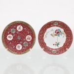 Dois(02) pratos de parede decorativos em porcelana chinesa de Jingdezhen, estilos Munshou e Família Rosa, circa meados do século XX. O primeiro exemplar apresenta esmaltação em fundo vermelho-coral com quatro medalhões brancos contendo os caracteres da inscrição auspiciosa "Wan Shou Wu Jiang" (Longevidade Infinita), intercalados por crisântemos e gavinhas em relevo (fencai). O segundo exibe centro branco com representação naturalista de ave policromada pousada em ramagem de peônia, circundado por aba ornamentada com motivos espiralados e florais sobre fundo vermelho idêntico. O reverso de ambas as peças revela base anelar em biscoito, marcas de fábrica carimbadas em tom vermelho com numerações de controle sob a inscrição "Made in China", e fixações artesanais superiores de passadores metálicos para suspensão em parede. Medidas: Diam.: 14,5cm.