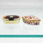 Duas(02) caixas de toucador, uma de formato quadrangular de cantos arredondados, em porcelana branca, com tampa abaulada, decoração floral policromada e ferragens em metal dourado, articulada por dobradiça e provida de fecho em forma de flor; e caixa oval em meterial plástico simulando metal dourado, com tampa revestida em material sintético de efeito tartaruga, medalhão circular aplicado ao centro e interior compartimentado. Ambas destinadas à guarda de pequenos objetos, joias ou acessórios de toucador. Medidas: Alt.: 3 x Comp.: 7 x Larg.: 5cm.Medidas: Alt.: 2,5 x Comp.: 7 x Larg.: 4cm.
