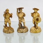 Três(03) figuras decorativas executadas em resina moldada de tonalidade marfim, segundo modelos derivados dos okimono japoneses difundidos durante o período Meiji. Representam personagens masculinos em indumentária tradicional: um trabalhador carregando tábua e ferramenta de carpintaria, outro portando bastão e chapéu de palha junto a elementos alusivos à pesca, e terceiro com amplo chapéu e objeto circular suspenso ao corpo. Figuras individualmente assentadas sobre bases ovaladas de superfície texturada. Medidas: Alt.: 8,5 x Comp.: 5 x Larg.: 4cm.