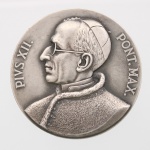 Medalha comemorativa em metal prateado, cunhada para o XXXVI Congresso Eucarístico Internacional, realizado no Rio de Janeiro em 1955. Anverso com busto em perfil do papa Pio XII, voltado à esquerda, acompanhado da legenda latina "PIVS XII  PONT. MAX.". Reverso com emblema do congresso, constituído por monograma cruciforme sobreposto por esfera armilar e elementos cruzados, circundado pela inscrição "XXXVI CONGRESSO EUCARISTICO INTERNACIONAL / RIO DE JANEIRO /1955". Na base da composição figura a assinatura "MONTINI". O congresso realizou-se no Rio de Janeiro em julho de 1955, durante o pontificado de Pio XII. Medida: Diam.: mm.