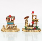 Duas(02) composições decorativas orientalistas, confeccionadas em materiais diversos, com figuras moldadas em material sintético de tonalidade marfim e elementos em metal, madeira e material plástico. Uma composição representa quiosque com figuras japonesas e lanternas vermelhas suspensas, acompanhado por cinco personagens dispostos diante da estrutura. A outra configura cena de jardim japonês, com figura feminina trajando quimono e portando sombrinha, poço, lanterna, treliça e luminárias esféricas vermelhas e branca. Bases ovais com tratamento simulando cercado de bambu. Medidas: Alt.: 9,5 x Comp.: 9,5 x Larg.: 5 cm. Medidas: Alt.: 8 x Comp.: 9,5 x Larg.: 5cm.