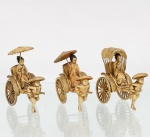Três(03) miniaturas de jinrikisha(riquixás) com figuras japonesas. Composições em material sintético de tonalidade marfim, com pátina castanha e detalhes policromados, representando tradicionais veículos japoneses de tração humana. Cada exemplar apresenta condutor masculino em movimento, com chapéu, puxando carro de duas rodas raiadas ocupado por figura feminina trajando quimono. Duas passageiras portam wagasa, tradicional sombrinha japonesa, enquanto a terceira se encontra sob cobertura arqueada e segura leque. Caixas dos veículos com laterais ornamentadas em relevo e, em um dos exemplares, espaldar decorado com paisagem japonesa representando o Monte Fuji, vegetação e construções. Elementos das vestes, rodas, assentos e coberturas trabalhados em relevo e incisão. Medidas: Alt.: 9 x Comp.: 9 x Larg.: 4cm.