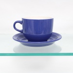 Xícara com pires em cerâmica vitrificada, corpo cilíndrico, asa lateral e respectivo pires circular, revestidos externamente por esmalte azul e internamente em branco. Conserva fragmentos de etiqueta comercial original no corpo. Medidas xícara: Alt.: 9 x Comp.: 15,5 x Larg.: 12cm.Medida pires: Diam.: 19cm.